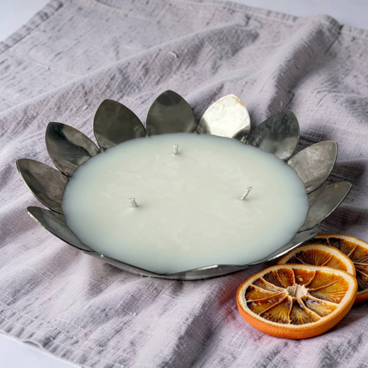 Candle in a metal holder with dried oranges on a textured fabric background