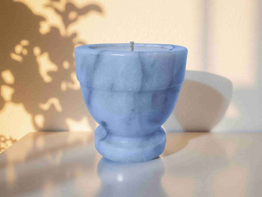 Blue marble-textured candle on a reflective surface with a blurred background