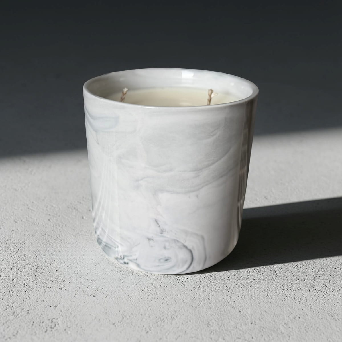 White marble-textured candle holder with a candle inside on a gray surface.