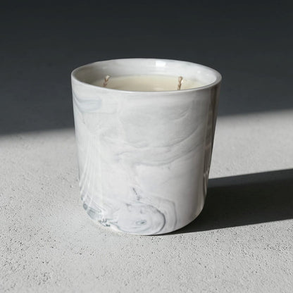 White marble-textured candle holder with a candle inside on a gray surface.