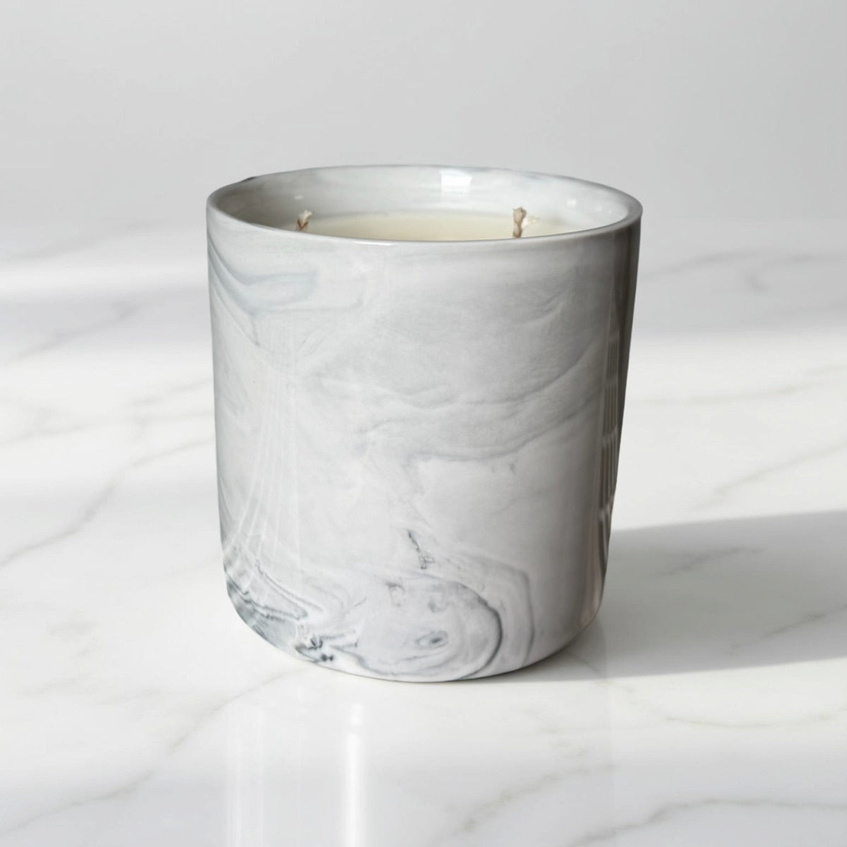 Marble-patterned candle in a glass container on a white marble surface