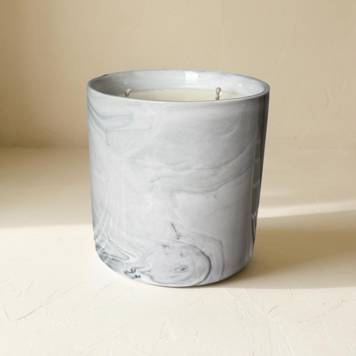 Marble-patterned candle in a gray container on a beige surface