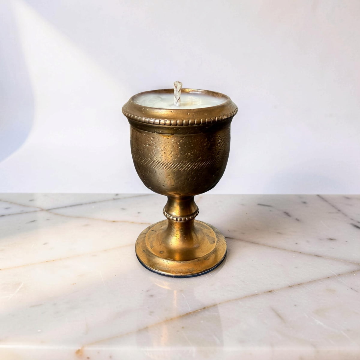Bronze candle holder with a lit candle on a marble surface