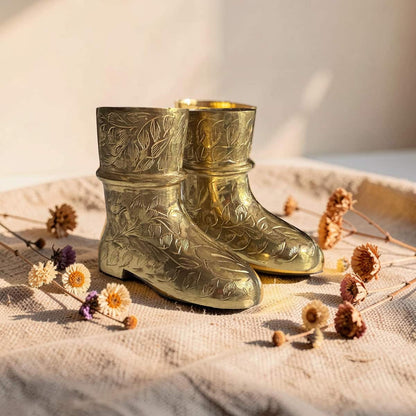 Pair of gold embossed boots on a textured surface with dried flowers.