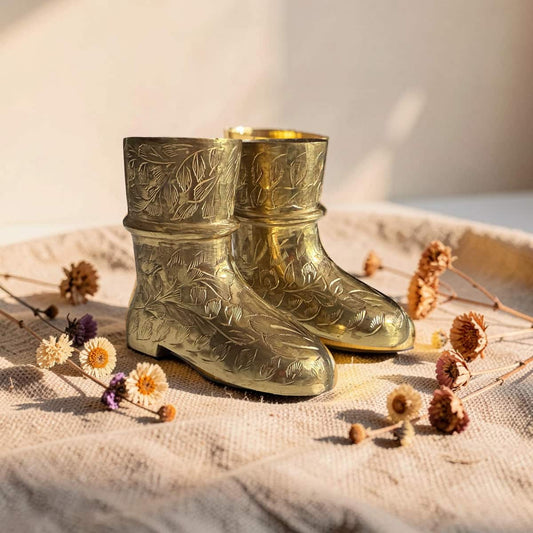 Pair of gold embossed boots on a textured surface with dried flowers.