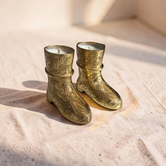 Two brass boot-shaped candles on a textured surface