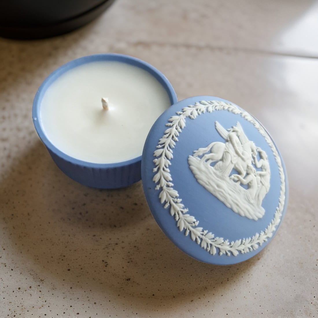 Candle in a decorative blue container with a white design on a speckled surface
