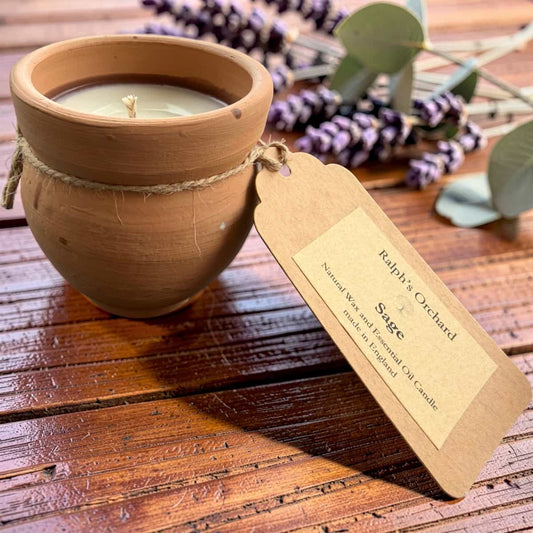 Candle in a terracotta pot with a tag on a wooden surface, surrounded by lavender flowers.