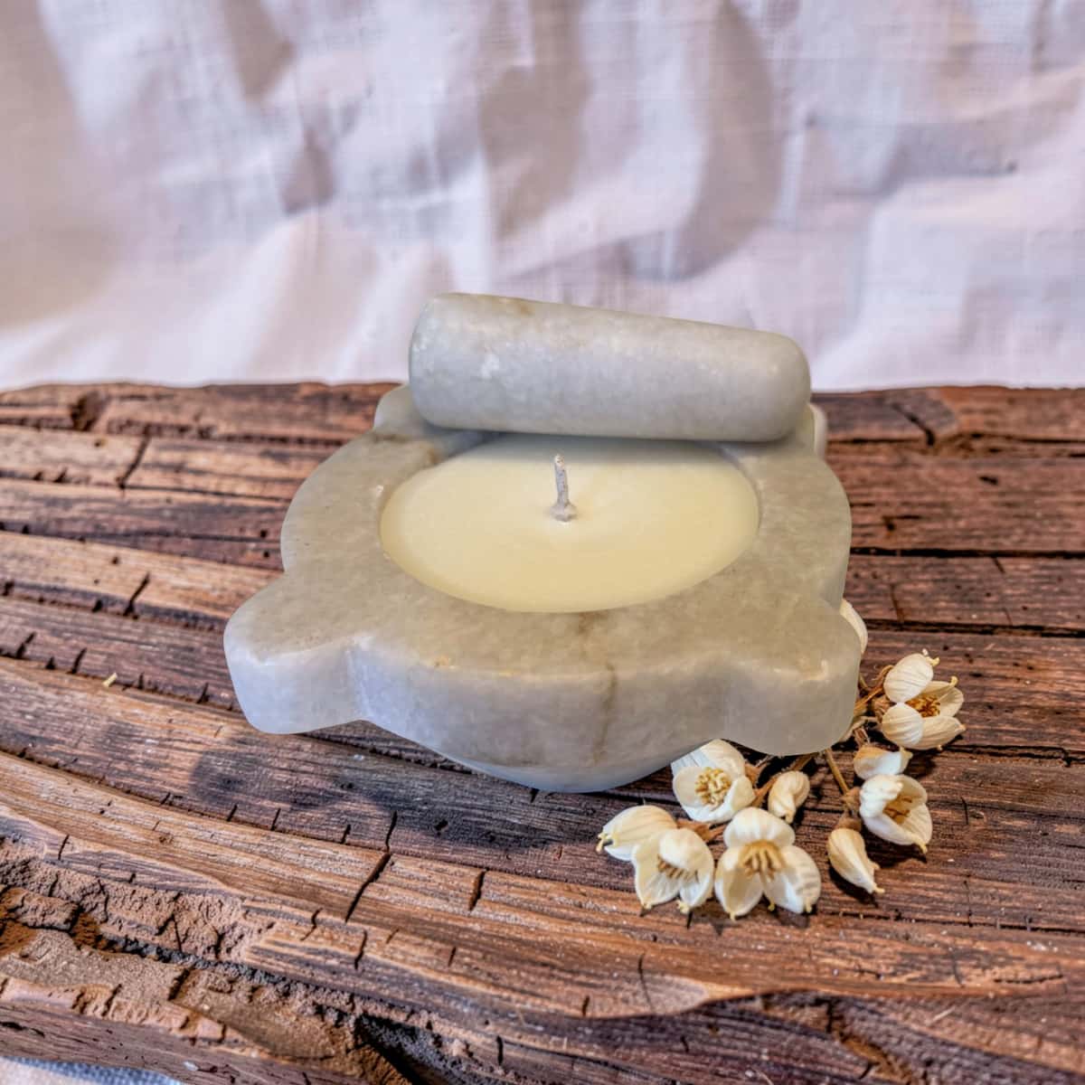 Candle in a stone holder on a wooden surface with white flowers