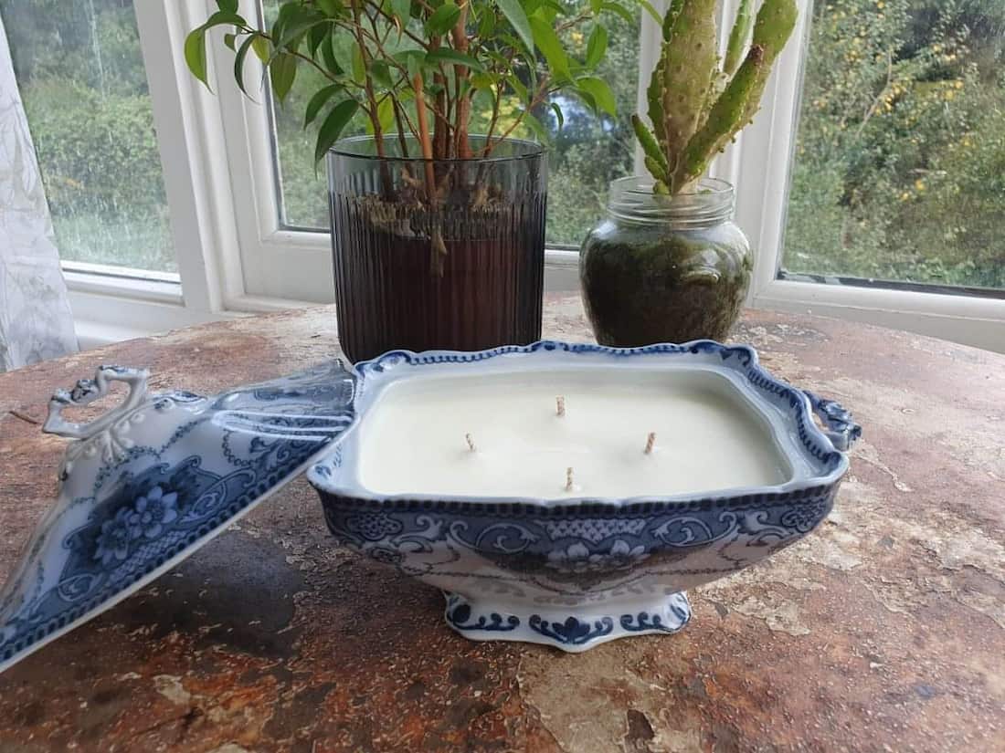 Candle in a decorative blue and white dish on a wooden surface with plants in the background.