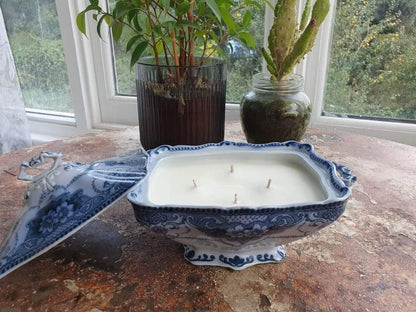 Candle in a decorative blue and white dish on a wooden surface with plants in the background.