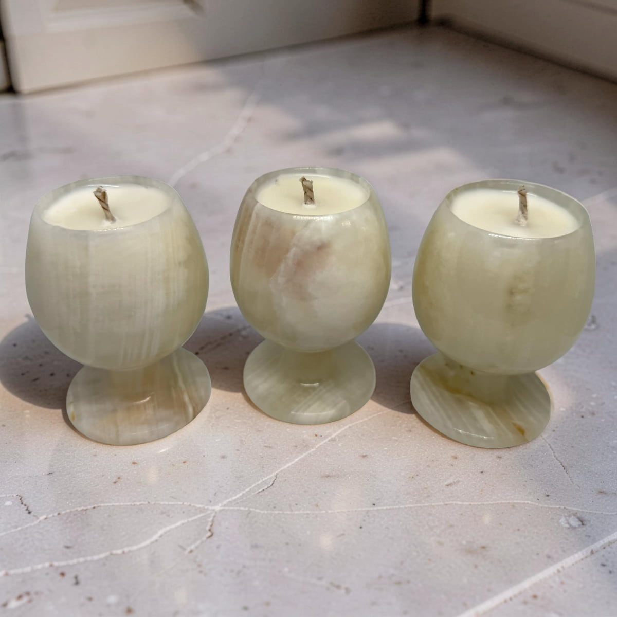 Three green onyx candle holders with candles on a light stone floor.