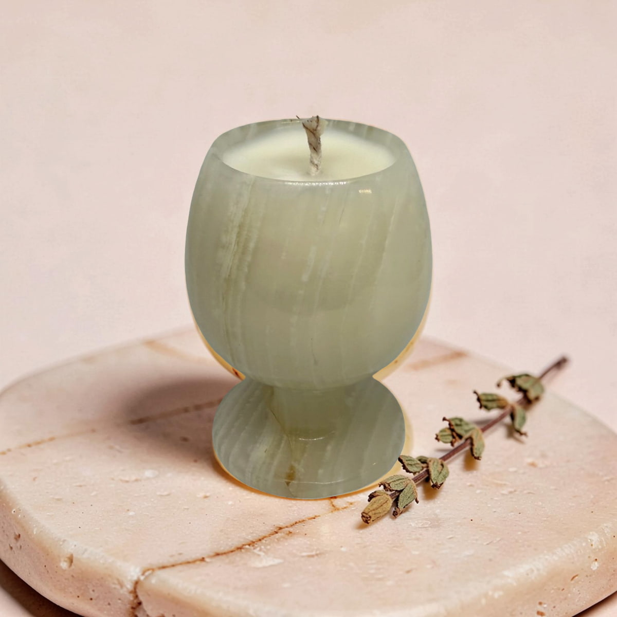 Green glass candle on a marble surface with a branch of herbs.