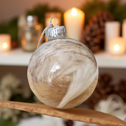 Decorative glass ball ornament with a marbled design on a wooden surface, with blurred candles and pinecones in the background.