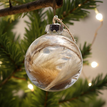 Clear glass ornament with feathers hanging on a Christmas tree branch.
