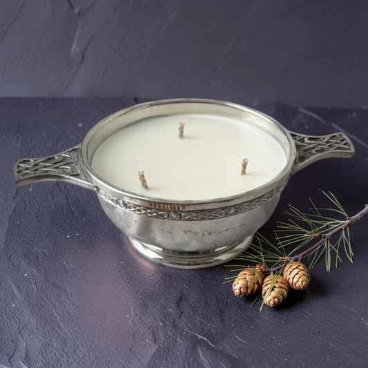 Decorative candle in a metal holder with pine cones on a dark surface