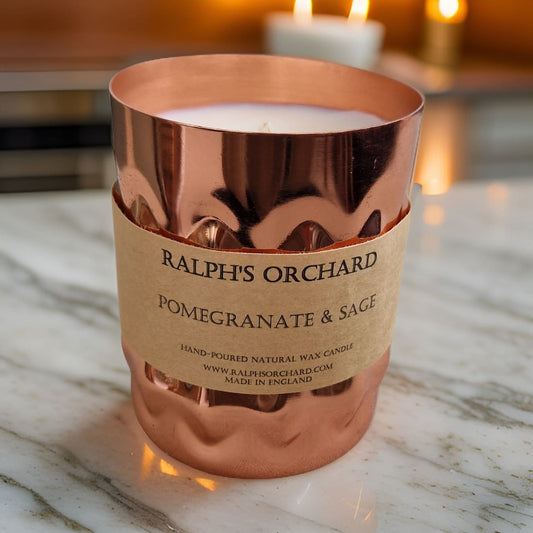 Candle in a rose gold holder with 'Ralph's Orchard' label on a marble surface.
