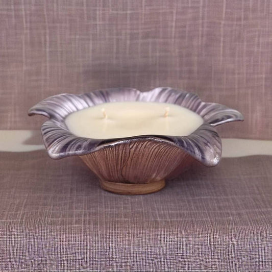 Candle in a decorative purple and brown ceramic holder on a textured surface