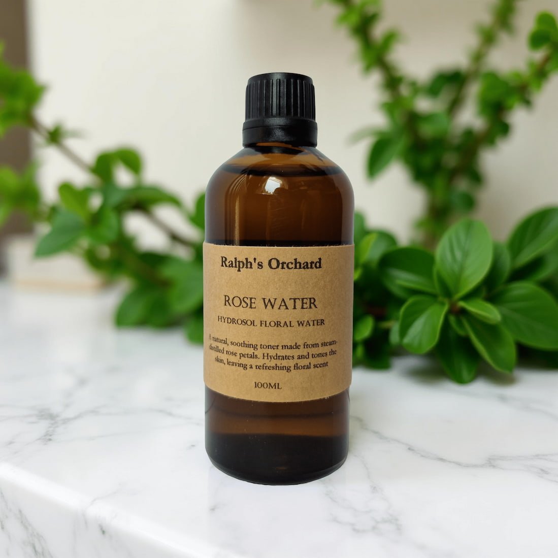 Bottle of Ralph's Orchard Rose Water on a marble surface with greenery in the background