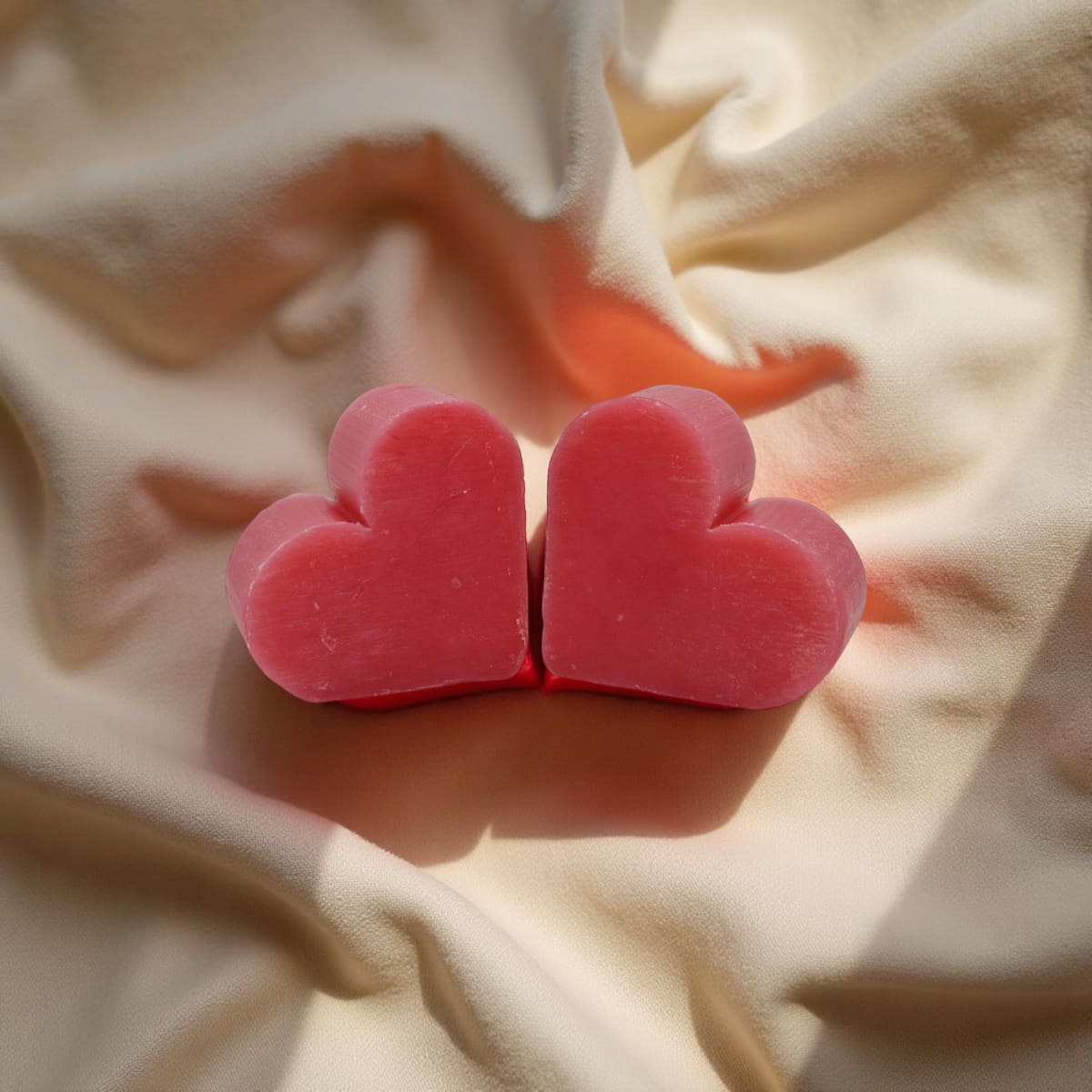 Two pink heart-shaped objects on a beige fabric background