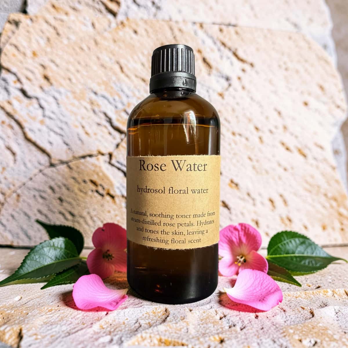 Bottle of rose water with flowers and leaves on a textured surface