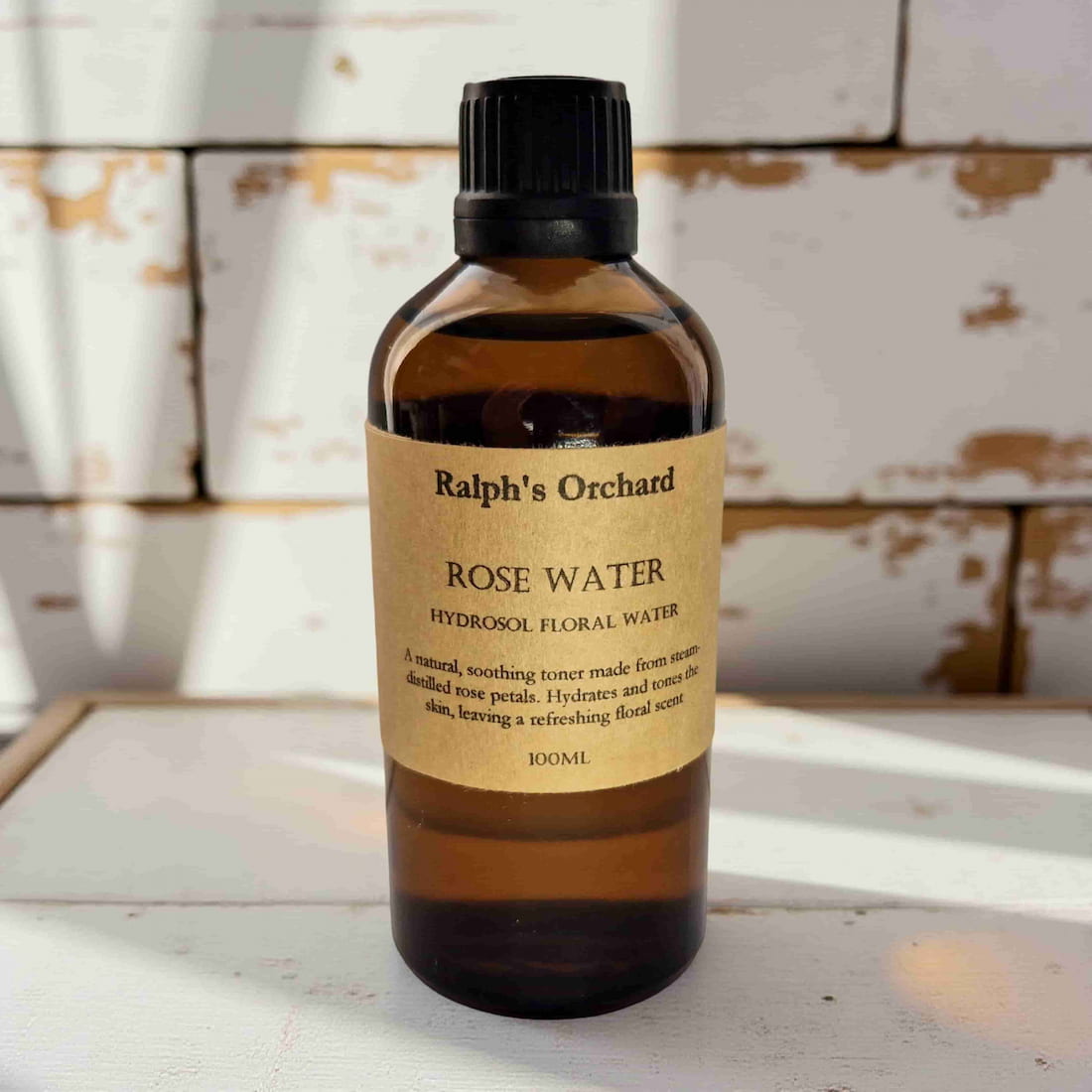 Bottle of Ralph's Orchard Rose Water on a wooden surface with a rustic background