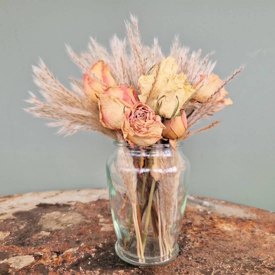 Glass vase with dried flowers on a textured surface against a plain background