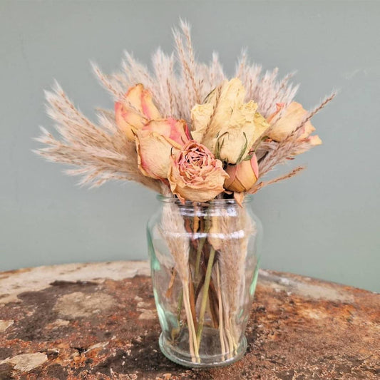 Glass vase with dried flowers on a textured surface against a plain background