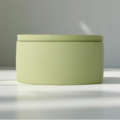 Green cylindrical container with a lid on a reflective surface with a blurred background