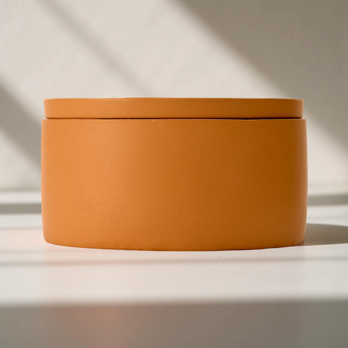 Orange cylindrical container with a lid on a light background