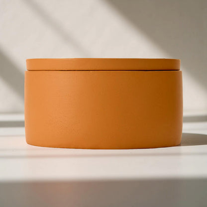 Orange cylindrical container with a lid on a light background