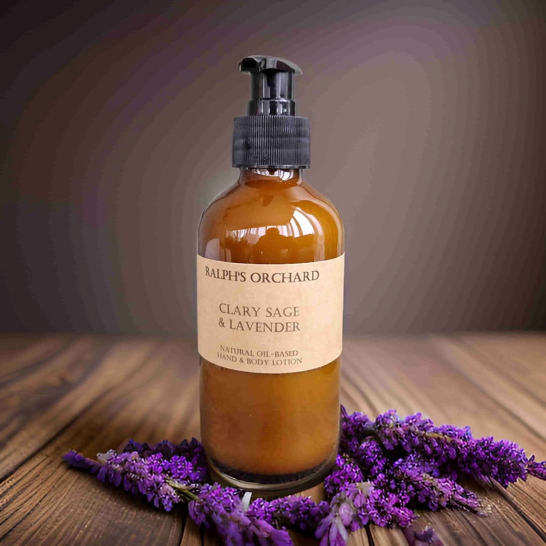 Bottle of Clary Sage & Lavender lotion from Ralph's Orchard on a wooden surface with lavender flowers.