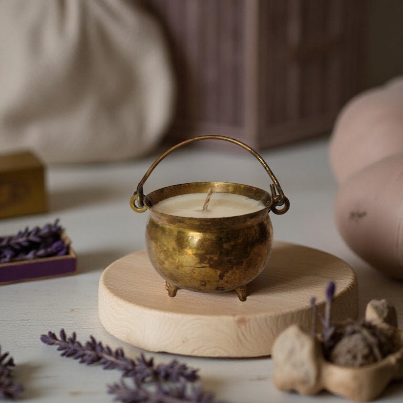 Brass candle holder with a lit candle on a wooden stand, surrounded by lavender and decorative items.