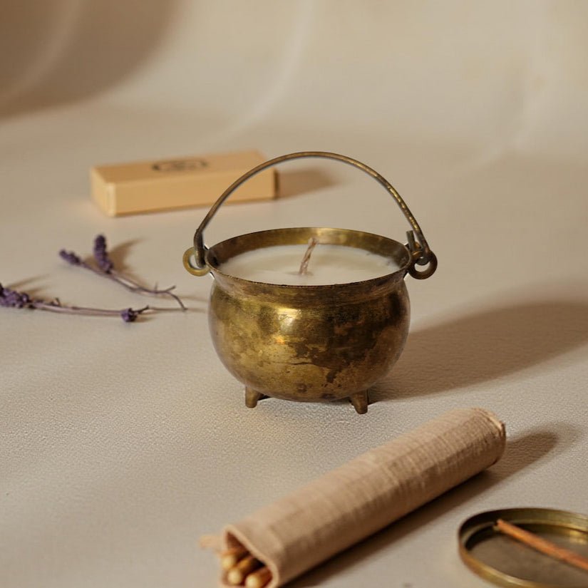 Brass candle holder with a candle, surrounded by lavender flowers and a rolled-up paper on a beige background.
