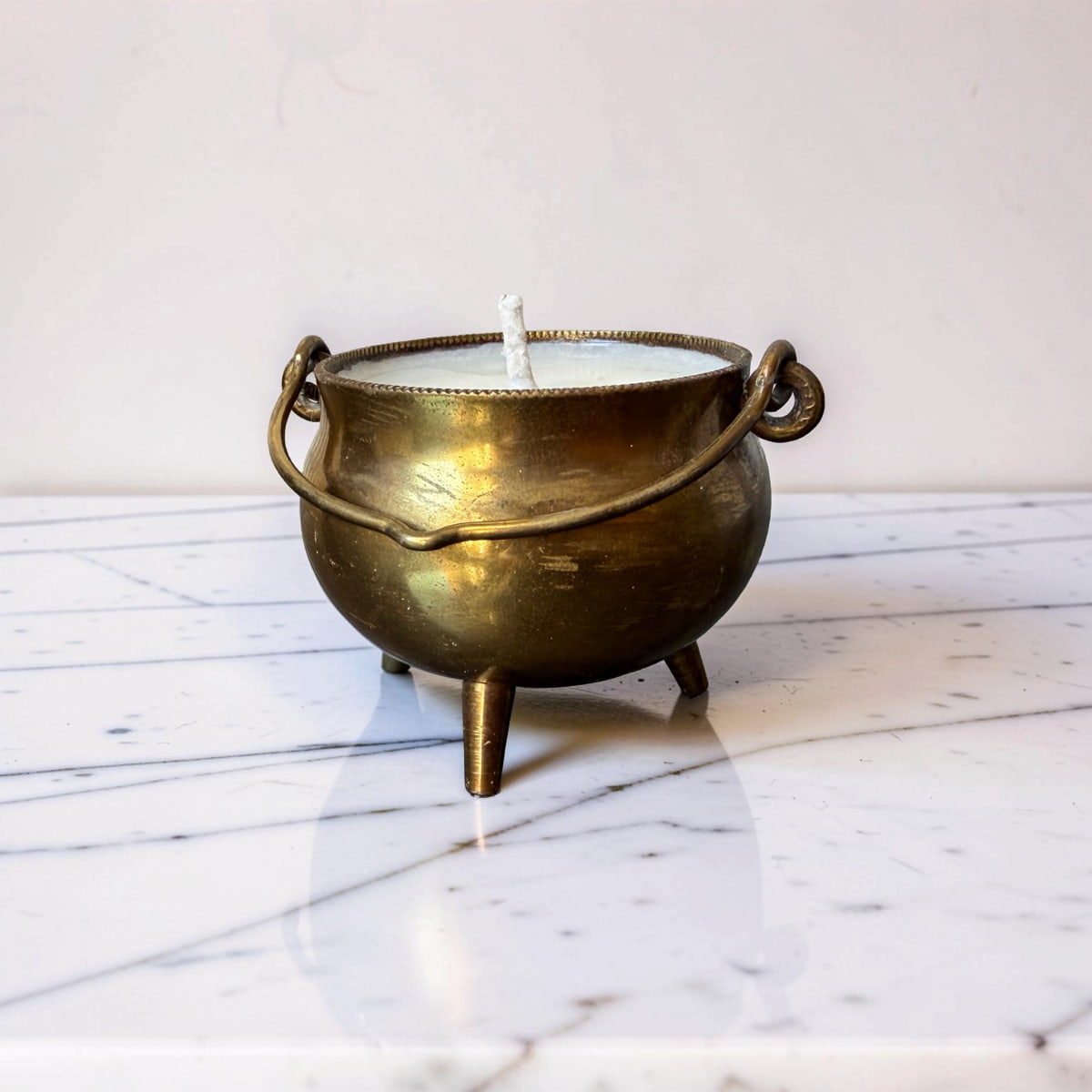 Brass cauldron candle holder with a white candle on a marble surface