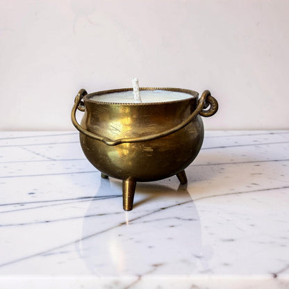 Brass cauldron candle holder with a white candle on a marble surface