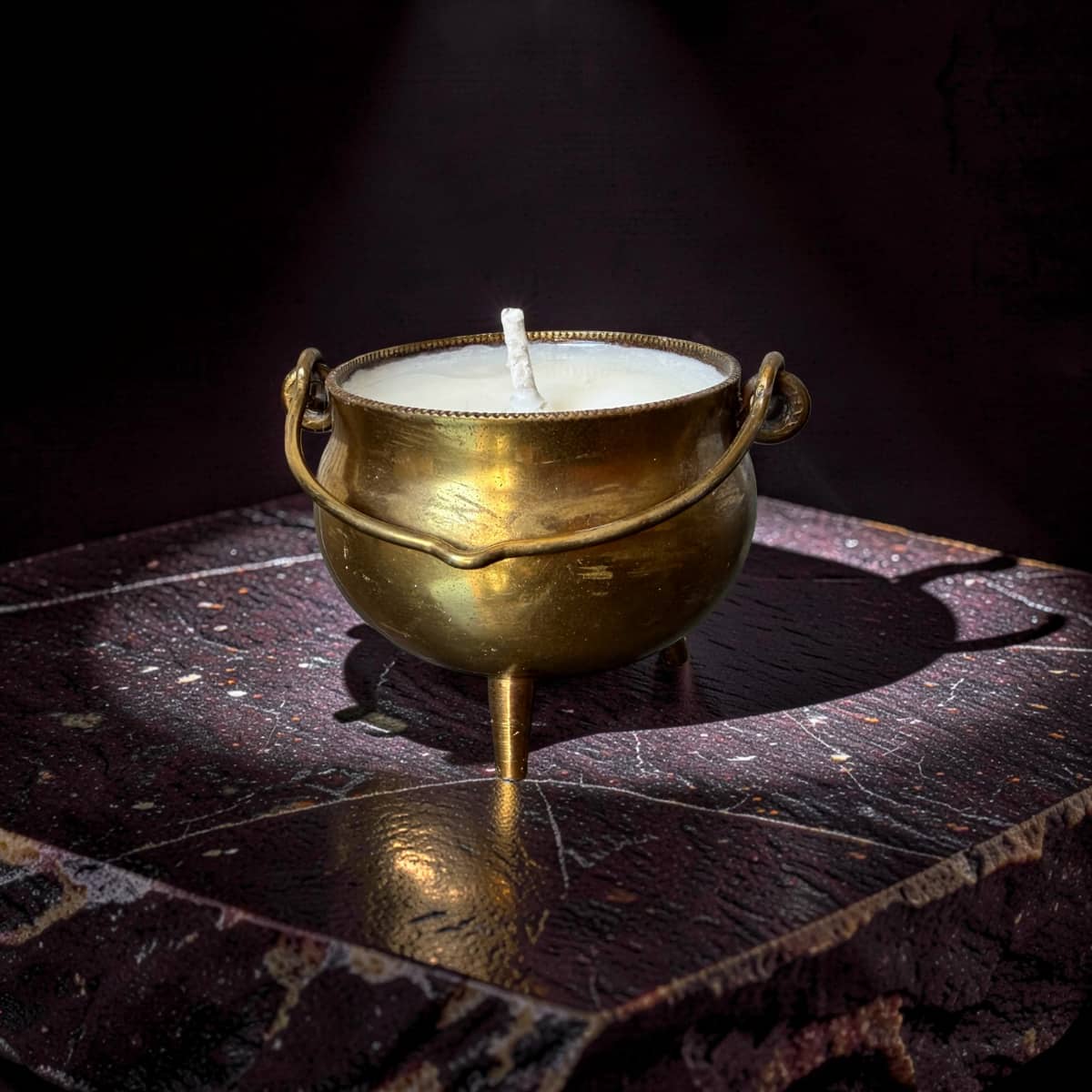 Candle in a brass cauldron on a dark surface