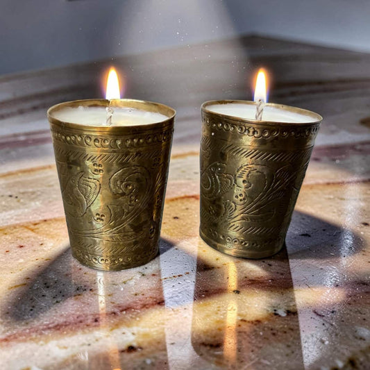 Two lit candles in ornate brass holders on a textured surface.