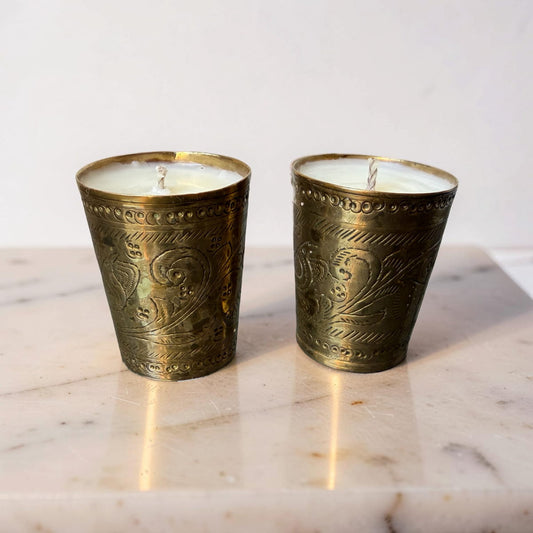 Two ornate brass candle holders with candles on a marble surface.