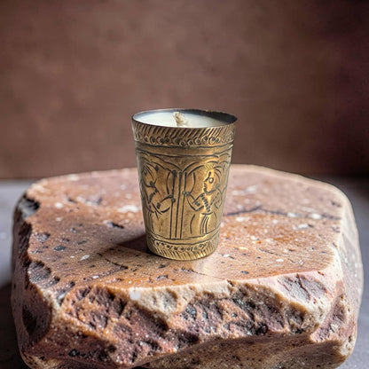 Decorative candle in an ornate brass holder on a stone surface with a brown background