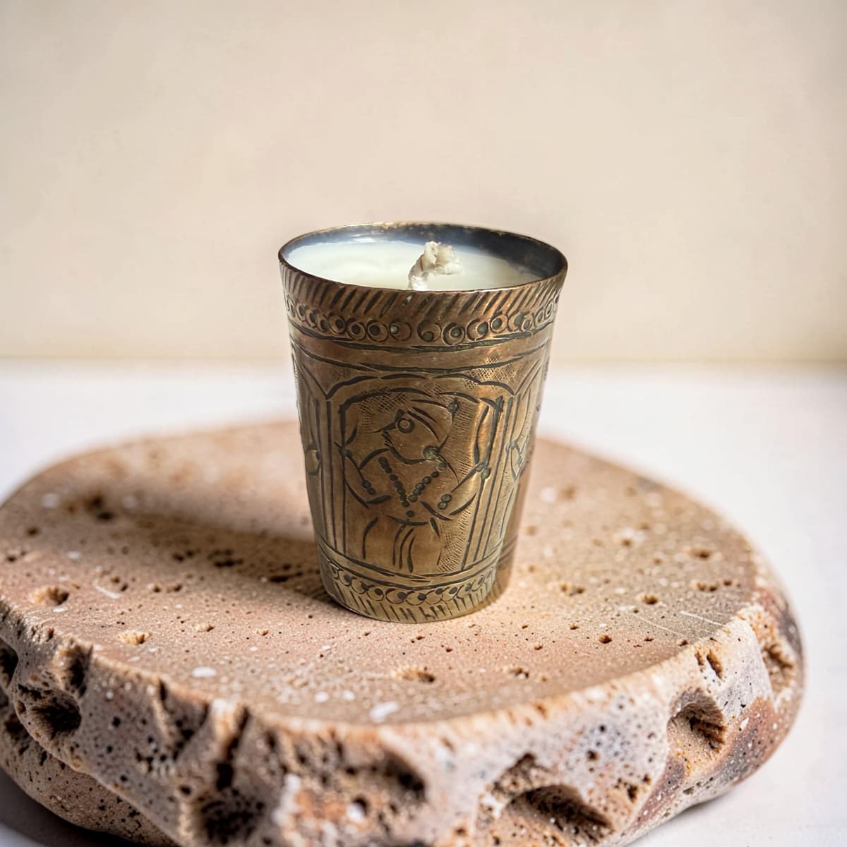 Decorative candle in an ornate metal holder on a textured stone surface with a neutral background