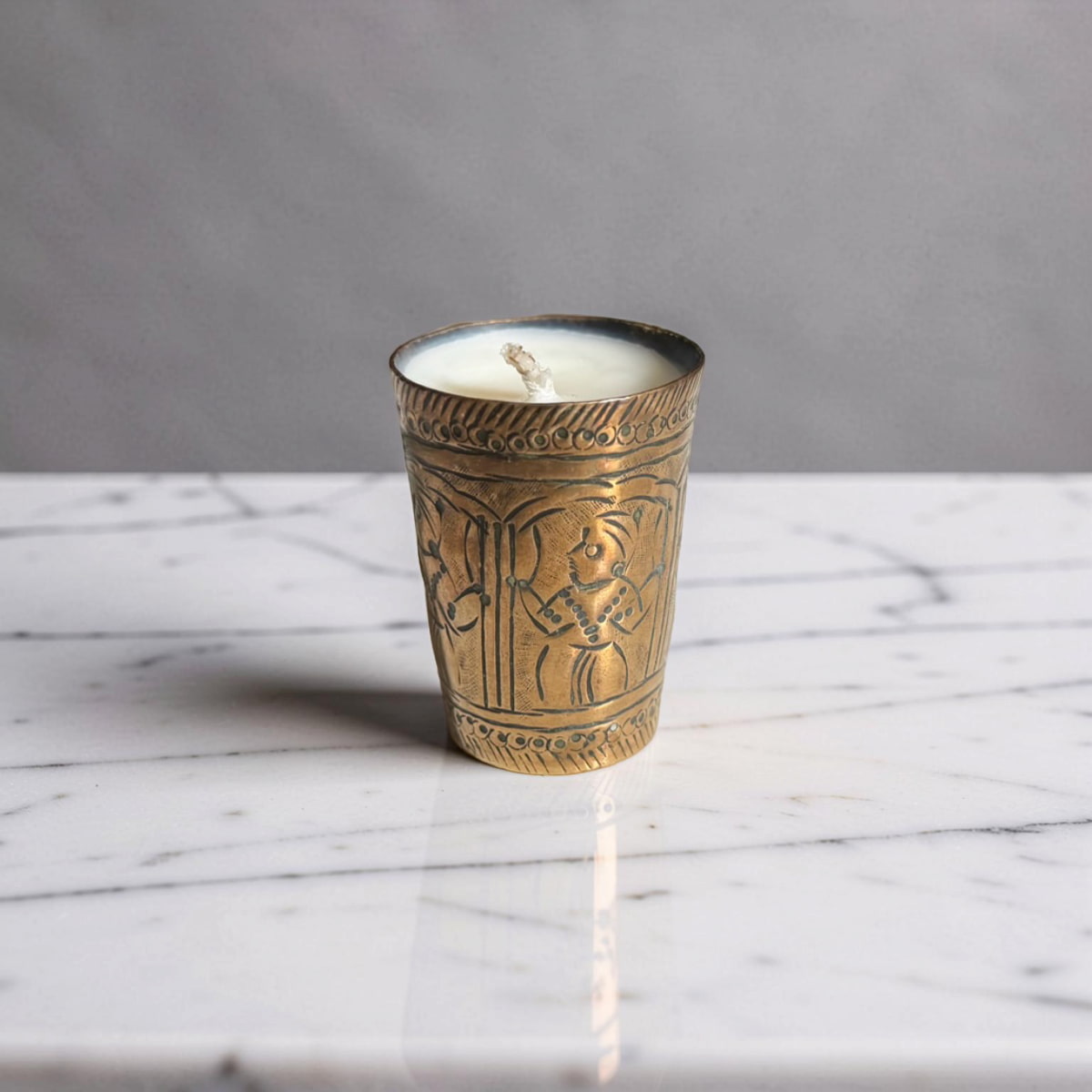 Decorative candle in an ornate brass holder on a marble surface with a gray background