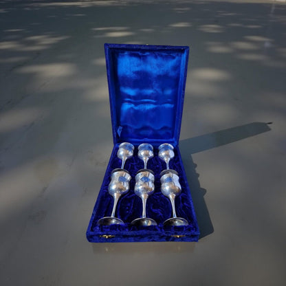 Set of six silver spoons in a blue velvet box on a reflective surface.