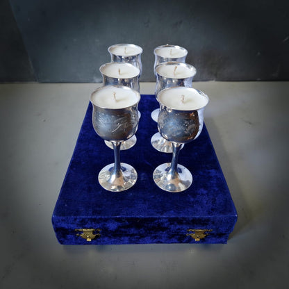 Silver wine glasses with candles on a blue velvet stand against a dark background