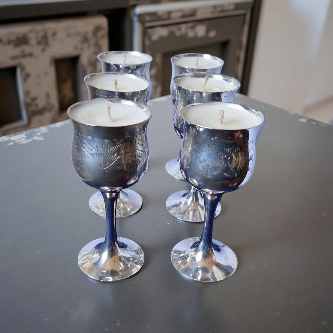Set of six silver goblet-shaped candles on a dark surface.