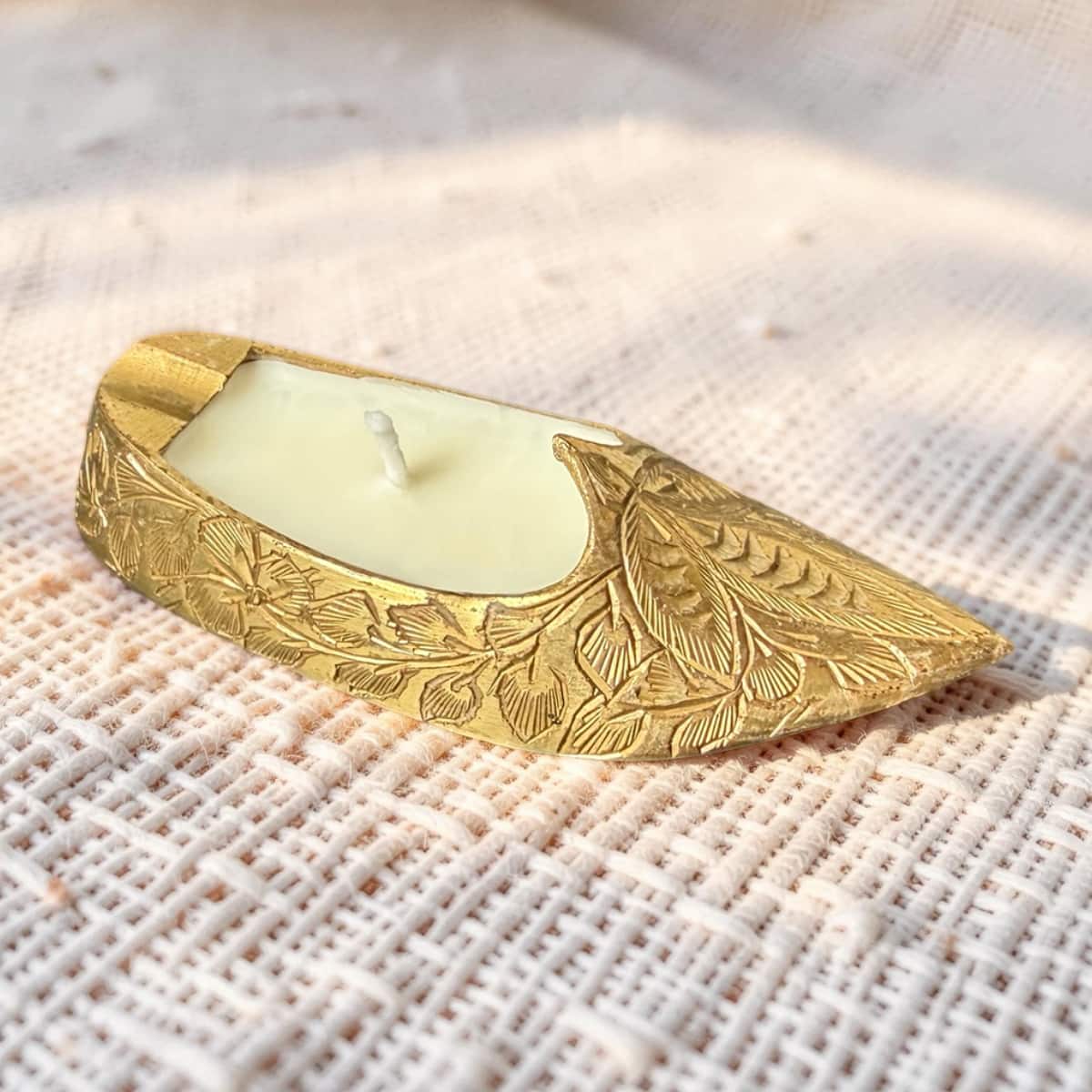 Decorative gold candle holder with a candle on a textured fabric background