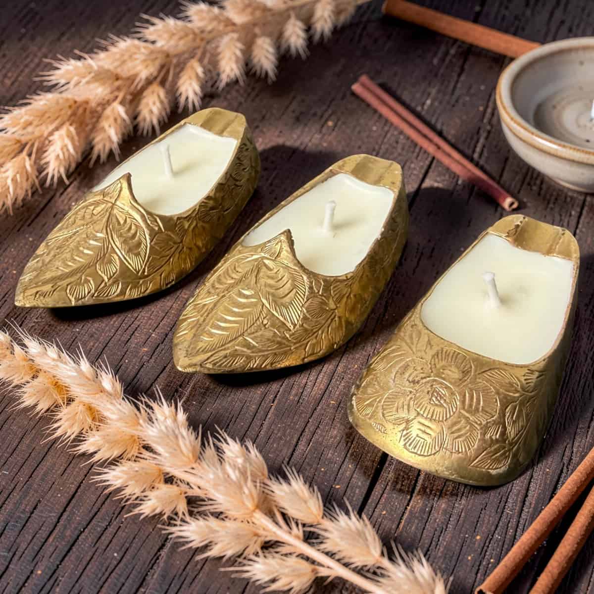 Three gold leaf-shaped candles on a wooden surface with dried plants and cinnamon sticks.