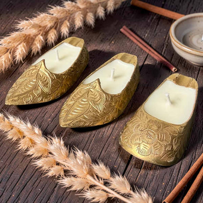 Three gold leaf-shaped candles on a wooden surface with dried plants and cinnamon sticks.