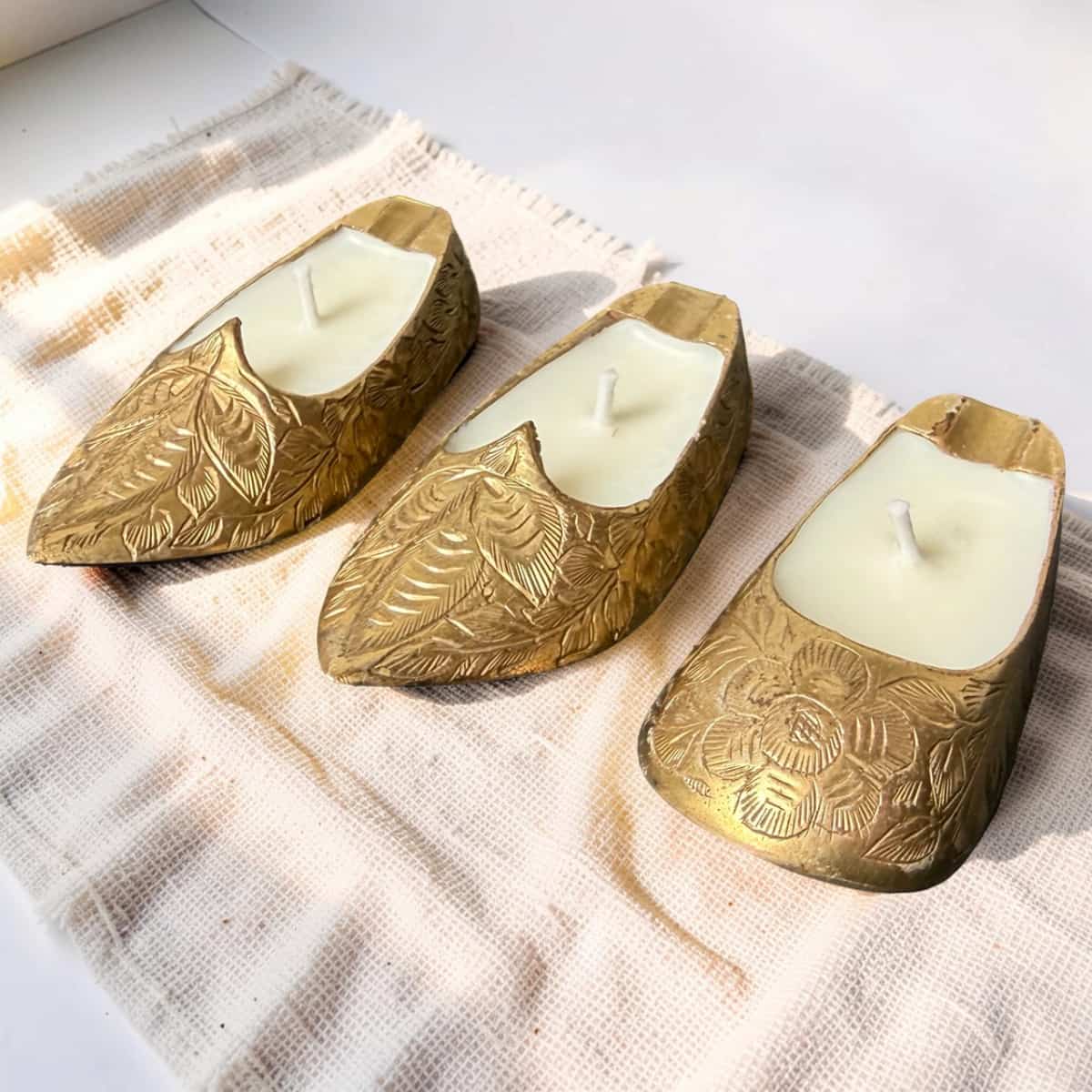 Three gold candle holders with white candles on a textured fabric surface