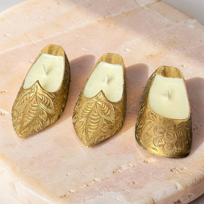 Three gold candle holders with white candles on a stone surface